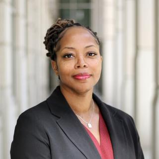 Headshot of Takiyah Golden where she is wearing a red blouse, black blazer, silver necklace with pendant and her hair in a braided bun.