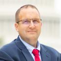 Mark Priebe standing in front of the U.S. Capitol. He's wearing a navy blue suit, red tie, and metal slate color eyeglasses.